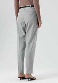 Grijze op maat gemaakte broek met een subtiele textuur, geplooide voorkant en een zwarte riem. De afbeelding toont de achterkant en een paar zwarte sandalen met hak.