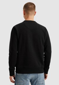 Černá mikina s kulatým výstřihem, pružnými manžetami a spodním lemem. Měkká tkanina; viditelné švy na rameni a zádech.