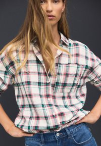 Camicia a quadri con bottoni nei toni del bianco, rosa e verde, dotata di tasca, taglio comodo e tessuto leggero. Indossata con jeans blu.