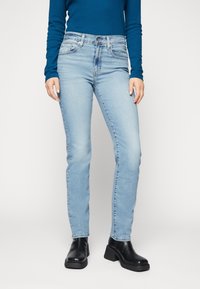 Jeans de pierna recta de color azul claro con una cintura de altura media, material de mezclilla, diseño de cinco bolsillos y detalles de desgaste sutiles. Combinados con botas negras de plataforma.