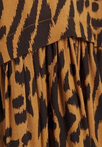 Brunt och svart djurtryckstyg med samlade veck och synlig diagonala sömmar.