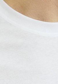 Biela bavlnená tričko s rebrovaným klasickým výstrihom. Tkanina sa zdá byť hladká a má jemnú textúru; detailný záber zdôrazňuje šitie.