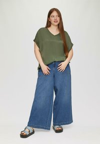 Zielony, krótki top z dekoltem w kształcie V; niebieskie dżinsy z szerokimi nogawkami; czarne sandały na platformie z jasnoniebieskim paskiem.