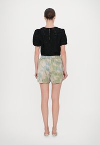 Zwarte kanten top met pofmouwen, gecombineerd met lichte shorts met een palmbladprint in groen en blauw op een beige achtergrond.