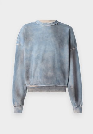 Sweatshirt bleu en tissu doux, avec un motif tie-dye légèrement décoloré. Il présente un col rond et des accents de pression en métal sur les manches.