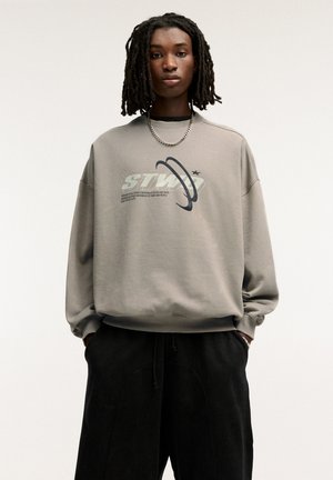 Gray oversized sweatshirt with a graphic design featuring rings and stars, made of soft fabric. Worn with black drawstring pants.