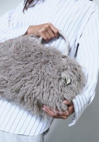 Sac à main gris fluffy avec une texture, de forme ronde et des poignées solides. Présente un charm en argent attaché à une des poignées.