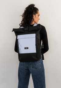 Black and light blue roll-top backpack with a front pocket, adjustable straps, and a label on the front, made of durable fabric.