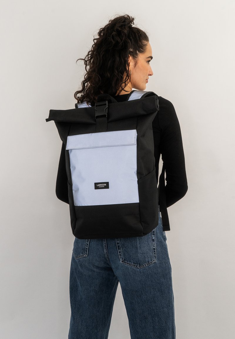 Black and light blue roll-top backpack with a front pocket, adjustable straps, and a label on the front, made of durable fabric.
