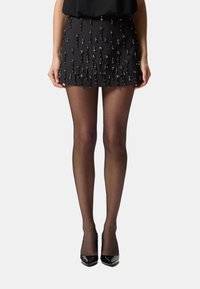 Minigonna nera con decorazioni verticali di perline, abbinata a calze nere trasparenti e tacchi alti neri lucidi.