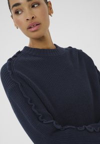 Navy blue knitted sweater featuring a ribbed crew neckline, textured fabric, and ruffled details along the sleeve seams.