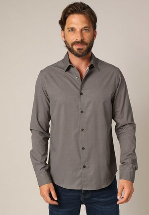 Chemise à manches longues à carreaux grise et noire, avec un col et des boutons foncés, associée à un jean bleu foncé.