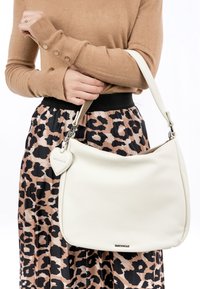 Weiße Ledertasche mit strukturiertem Oberflächen, einem Schultergurt und einem herzförmigen Anhänger. Kombiniert mit einem Leopardenmuster-Rock und einem braunen Pullover.