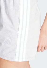 Pantaloni scurți atletici de culoare gri deschis, confecționați dintr-un material moale, cu dungi laterale albe și un logo brodat în partea stângă jos.