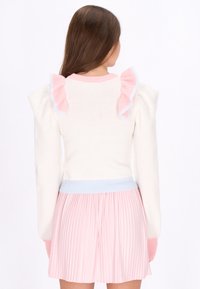 Maglione crema con accenti ruffled rosa, caratterizzato da una vita a costine blu. Gonna plissettata rosa chiaro completa l'outfit. Tessuto texture.