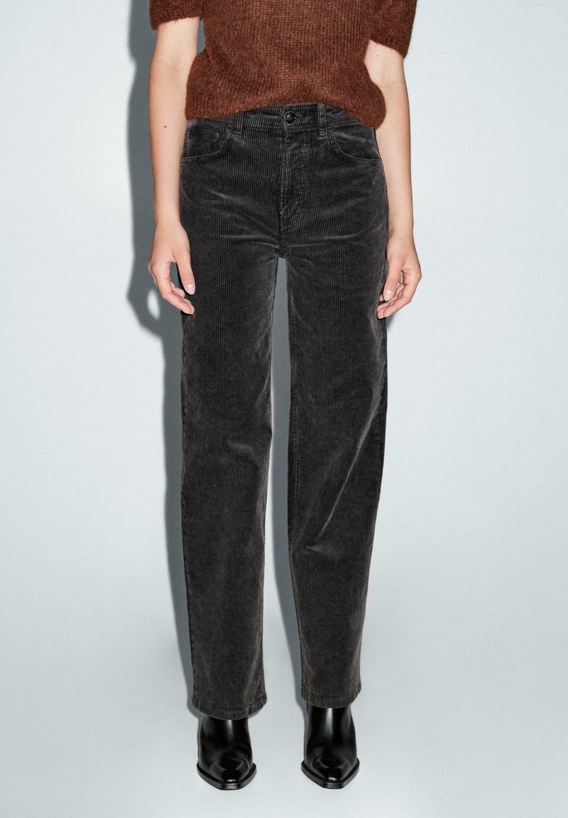 Pantaloni in corduroy neri con gamba dritta, caratterizzati da una vita alta, tasche frontali e delicate righe verticali. Abbinati a stivali neri alla caviglia.