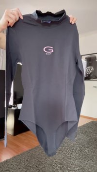 Sötét szürke, hosszú ujjú body magas nyakkal, amelyet a kezek tartanak, az elülső részen rózsaszín "G" és "GANT" logóval.