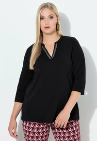 Black V-neck top with three-quarter sleeves, featuring a decorative silver accent along the neckline. Paired with patterned pink and black leggings.