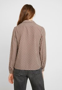 Blusa stampata in tessuto leggero, caratterizzata da un design geometrico rosso e crema, maniche lunghe e colletto. 