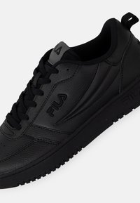 Chaussures de sport noires avec une tige en cuir texturé, bout rond et col rembourré. Elles sont dotées de lacets noirs et d'un logo sur le côté.
