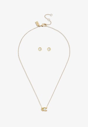 Halskette in Goldfarbe mit einem runden Anhänger, der einen klaren Kristall zeigt. Enthält passende runde Steckerohrringe, beide minimalistisch und elegant.