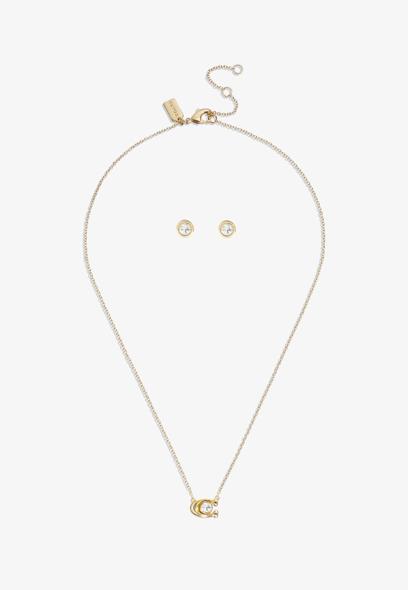 Smykke i guldfarvet med et cirkulært vedhæng, der har en klar krystal. Inkluderer matchende runde studørekroge, begge minimalistiske og elegante.