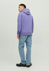 Felpa viola con tasca a canguro, polsini e orlo a coste, abbinata a jeans azzurri chiari e scarpe nere, vista da dietro.