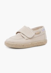 Scarpa di tela beige con cinturino in Velcro, punta rotonda e suola in juta intrecciata; presenta un piccolo etichetta sul lato e una parte superiore testurizzata.
