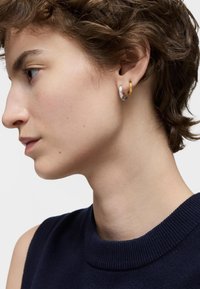 Pendientes de aro de plata y oro, con un diseño simple y moderno. El aro de plata es más ancho, mientras que el aro de oro es un acento más delgado.