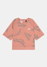 Tričko s krátkým rukávem a kulatým výstřihem v světle broskvové barvě, s šedými zakřivenými textovými vzory a logem adidas na přední straně. Měkká, lehká tkanina.