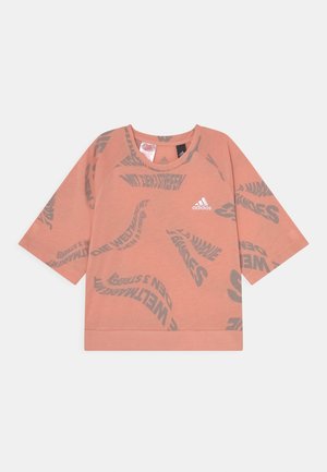 Tričko s krátkým rukávem a kulatým výstřihem v světle broskvové barvě, s šedými zakřivenými textovými vzory a logem adidas na přední straně. Měkká, lehká tkanina.