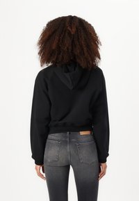 Black cropped hoodie with a hood, featuring raglan sleeves. Paired with gray fitted jeans showing a subtle fade and back pockets.