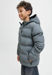 Grå puffjacka med huva, med kviltad detaljering, dragkedja fram och sidofickor, bärs över mörka jeans.