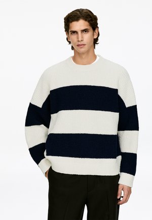 Knit sweater with horizontal stripes in cream and navy, rounded neckline, and relaxed fit. Long sleeves with ribbed cuffs.