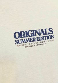 Cotton t-shirt in light beige with navy blue printed text reading "ORIGINALS SUMMER EDITION" and additional smaller text below.