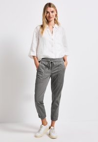 Ljus linneknäppningsskjorta i vitt, parat med grå tapered byxor med elastisk midja och fickor. Stylad med vita sneakers.