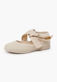Scarpa in tessuto beige con tomaia texturizzata, punta arrotondata e cintura regolabile con fiocco alla caviglia per la chiusura. Suola piatta.