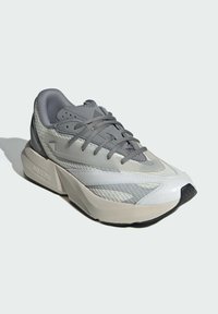 Harmaa urheilukenkä, jossa on teksturoitu verkko-osa, kontrastiväriset sileät yksityiskohdat, litteät nauhat ja massiivinen, muovattu pohja mustilla yksityiskohdilla.