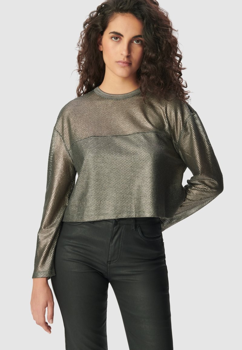 Metallic-Gitter Langarmoberteil mit einem verkürzten Design, das eine solide Unterlinie aufweist, ergänzt durch enganliegende schwarze Hosen.