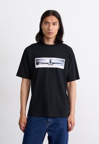 Sort bomulds T-shirt med et centralt grafiktryk af en figur, der holder en basketball. Korte ærmer og afslappet pasform.