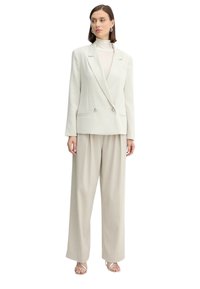 Blazer doppiopetto color beige chiaro con due bottoni metallici, abbinato a pantaloni a gamba larga dello stesso colore e décolleté con cinturini argentati.