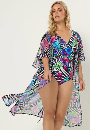 Donna che indossa un costume da bagno con stampa floreale e zebra, abbinato a un copricostume trasparente, posando davanti a uno sfondo chiaro uniforme.