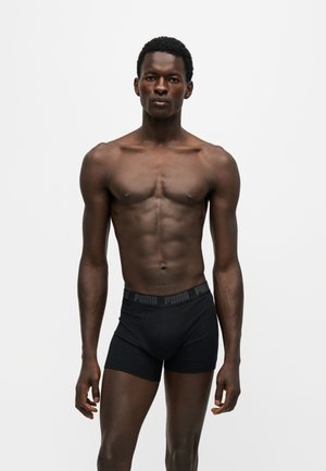 Homme athlétique debout face à l'avant portant un boxer noir Puma sur fond blanc uni.