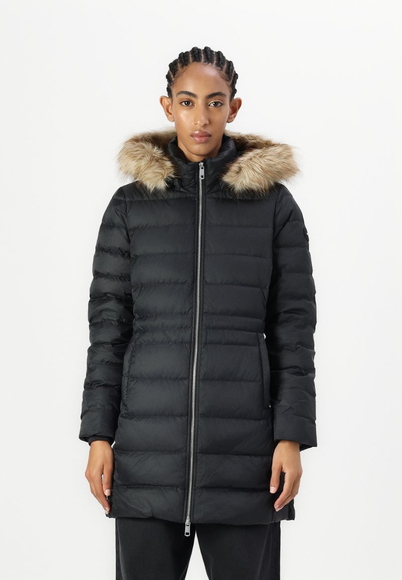 Crni zimski kaput s perjem i odvojivom umjetnom krznom na kapuljači, prednjim zatvaračem i osjećajem prekrivene teksture. Dugi rukavi i podesiv struk.