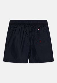 Pantaloni da nuoto blu navy con vita elastica e una tasca posteriore dotata di un occhiello rosso a contrasto. Tessuto leggero e liscio.