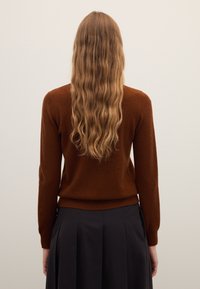 Brown sweater made of soft material, fitted design with long sleeves, rounded neckline, and ribbed hem, worn with a black skirt.