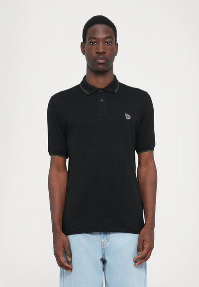 Zwarte polo met korte mouwen en een groene kraagtrim. Heeft een klein geborduurd ontwerp op de linkerborst. Glad katoenmateriaal.