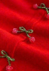 Roter gestrickter Stoff mit mit Perlen verzierten Blumenakzenten in Pink und grünen Blattformen. Nahaufnahme zeigt die Textur und Verzierungen.