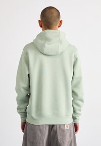 Huvtröja i ljusgrön färg, tillverkad av mjukt material. Har en avslappnad passform, ribbade muddar och nederkant, med en logotyp på den nedre sidan.