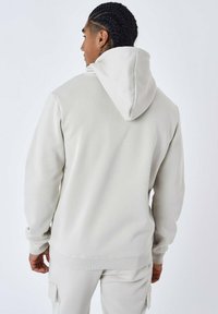 Sudadera con capucha de color gris claro, hecha de tejido suave, con un corte relajado, puños acanalados y un bolsillo tipo canguro en la parte delantera.